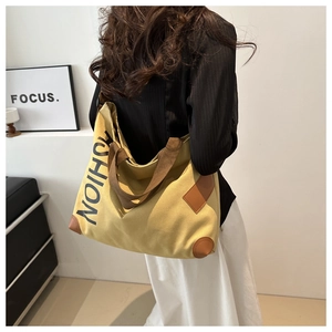 Detail of yellow canvas tote bag featuring FASHION print and brown leather corner patches