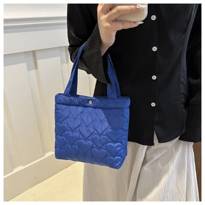 Detail of royal blue quilted tote bag with heart patterns and gold metal button