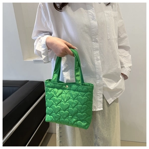 Detail of green heart-quilted nylon tote bag featuring a gold metal snap button closure