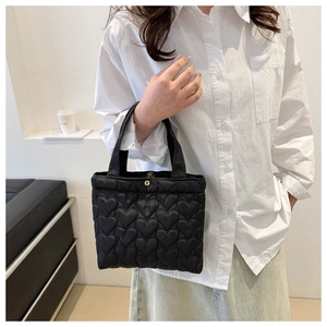 Detail of black quilted tote bag featuring heart pattern stitching and gold magnetic closure
