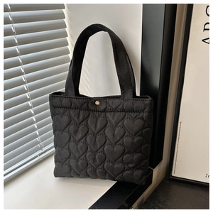 Detail of black heart-quilted nylon tote bag featuring a golden snap button closure
