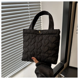 Detail of black quilted tote bag featuring heart pattern embroidery and gold button closure
