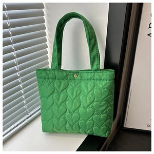 Close-up of green tote bag featuring heart-shaped quilting and a gold snap button closure