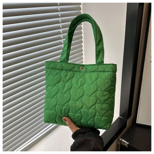 Close-up of green tote bag featuring heart-shaped quilting and a gold snap closure