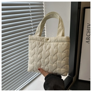 Detail of cream quilted tote bag featuring heart pattern texture and gold button closure