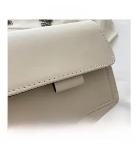 Detailed macro view of cream-white leather texture and dark gray metal chain on crossbody bag