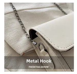 Detail of white lychee leather texture and metallic ring hook on a minimalist square bag
