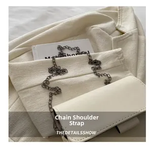 Detail of minimalist cream leather crossbody bag with dark grey metal chain strap