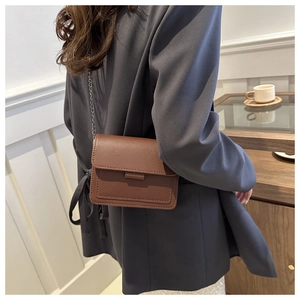 Elegant brown faux leather crossbody bag with metal chain strap shown in a lifestyle setting
