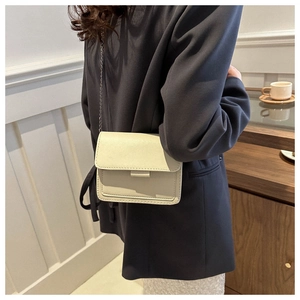 Detail of cream white leather crossbody bag with silver metal chain strap on model