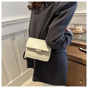Close-up of a cream-colored crossbody bag with metal chain strap worn on navy blue suit