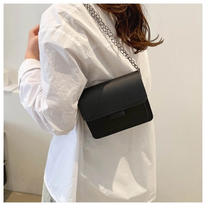 Detail of minimalist black PU leather flap bag with dark metallic chain strap on model