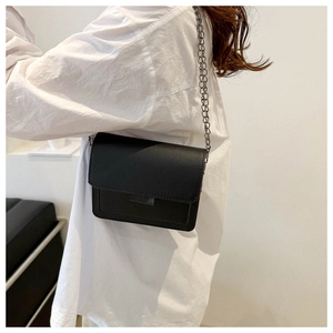 Detailed view of a sleek black leather crossbody bag with silver chain strap on a model