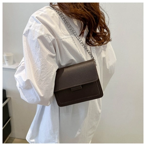 Detail of dark brown flap crossbody bag with silver chain strap on white shirt