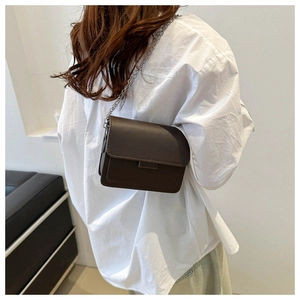 Detail showing deep brown faux leather crossbody bag with silver chain strap on a model