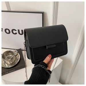 Close-up of minimalist black square crossbody bag with metal chain strap and flap
