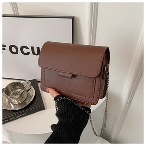 Brown faux leather crossbody bag detail featuring white stitching and silver chain strap
