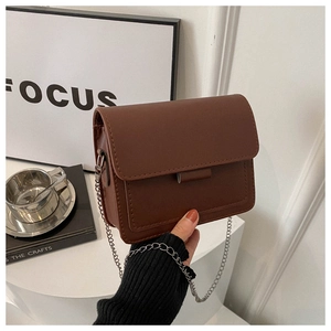 Detailed view of a brown matte leather crossbody bag with metal chain strap held by hand