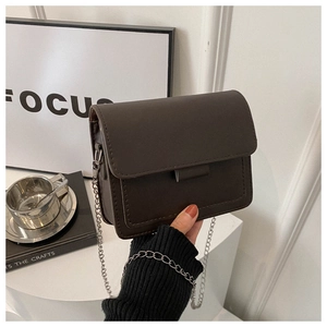 Close-up of dark brown leather crossbody bag with silver chain and fine stitching