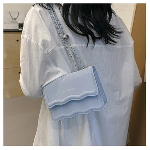 Detail of light blue leather handbag with wave edge flap and silver chain strap