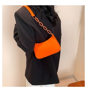 Detail of orange crocodile pattern bag with thick chain strap worn over black suit