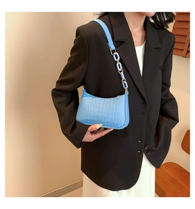 Detail of light blue baguette bag with crocodile texture and decorative chain strap