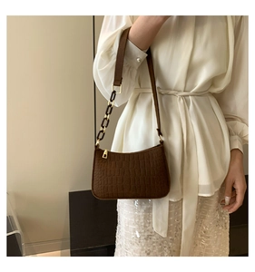 Close-up of dark brown crocodile pattern baguette bag with stylish chain detail