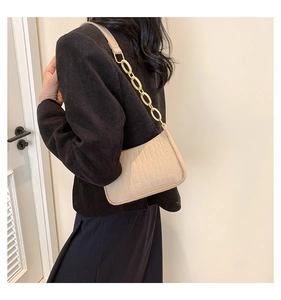 Detail of beige crocodile embossed baguette bag with gold chain strap on model shoulder