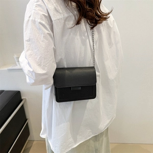 Minimalist black leather crossbody square bag with chain strap worn on white shirt