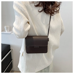 Borsa a tracolla marrone scuro minimalista su modella con elegante abito bianco