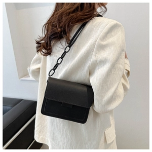 Dettaglio borsa a tracolla nera minimalista con finitura opaca e catena su un blazer bianco