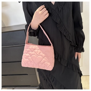 Détail d'un sac à main matelassé rose avec motifs de cœurs sur fond de robe noire