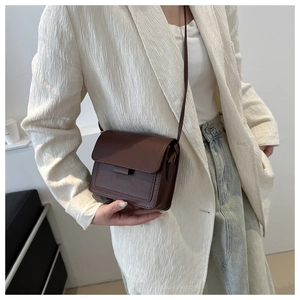 Dettaglio di una borsa mini quadrata in pelle marrone scuro indossata con un blazer