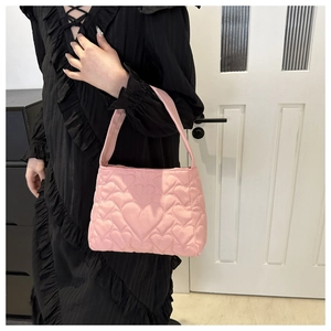 Sac à bandoulière matelassé cœur rose porté sur l'épaule sur fond d'intérieur minimaliste