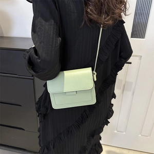 Dettaglio di una piccola borsa a tracolla verde chiaro indossata da una modella in interni