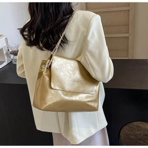Close-up of golden crossbody bag with chain strap and pleated texture on model