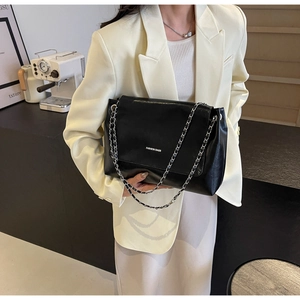 Detail of black glossy leather tote bag with silver chain strap and fashion lettering