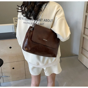 Detail of dark brown leather tote bag with metal chain strap and fashion logo