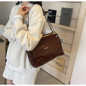 Detailed view of the dark brown glossy leather texture and silver chain strap on the bag