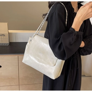 Detail view of large cream PU leather tote with silver chain strap on model shoulder