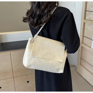 Detail of a beige leather crossbody bag with silver chain strap worn by a model