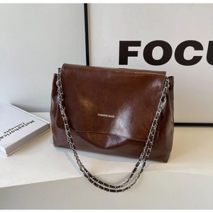Detail of dark brown glossy leather crossbody bag with silver chain strap and fashion logo
