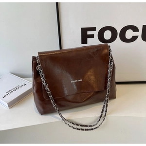 Macro view of vintage brown oil-wax leather texture and silver chain strap on tote bag
