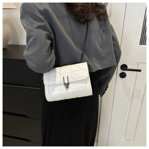 Détail du sac matelassé blanc avec fermoir en métal porté sur une veste grise chic