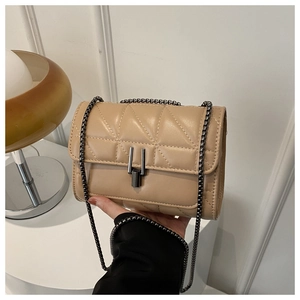 Gros plan d'un sac bandoulière matelassé beige avec fermoir métallique et chaîne à la main