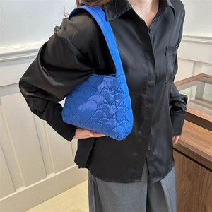 Sac à main bleu Klein matelassé avec motifs de cœur porté par un mannequin