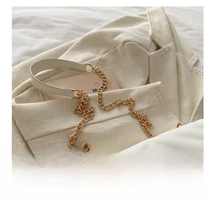 Detail of white quilted handbag with gold metal chain strap on a beige blazer background
