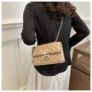 Detail of beige quilted shoulder bag featuring a gold clasp and metal chain strap