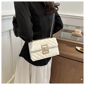 White quilted crossbody bag with gold chain strap shown in a chic cafe setting