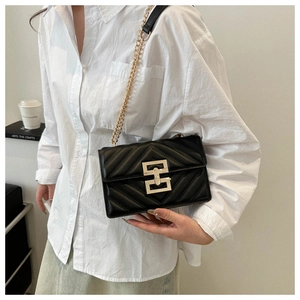 Detail of black quilted crossbody bag with gold hardware worn with a white shirt